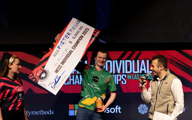 A student holds an oversized prize cheque on stage after winning the MECC individual championship.