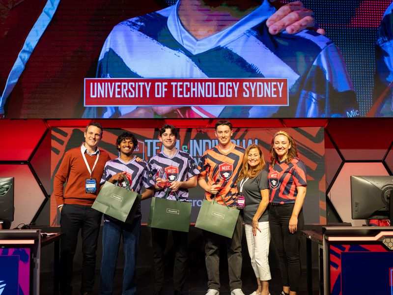 The University of Technology Sydney team on the championship stage, their school name on the screen behind them.